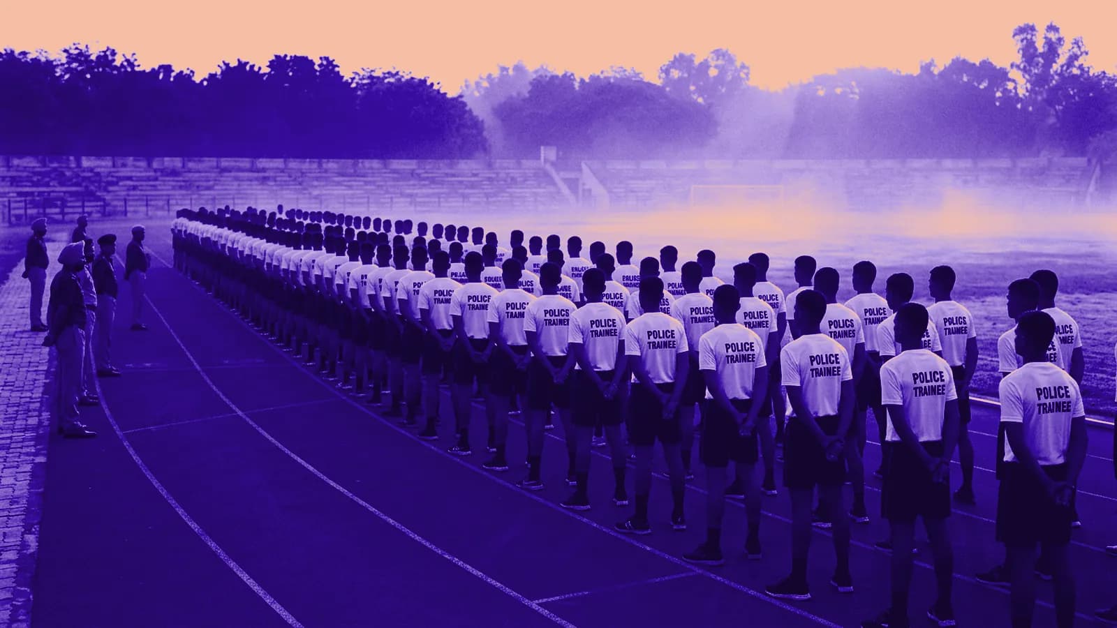 Police constable recruits in athletic PT gear lined up at outdoor stadium red running track in early sunrise mist