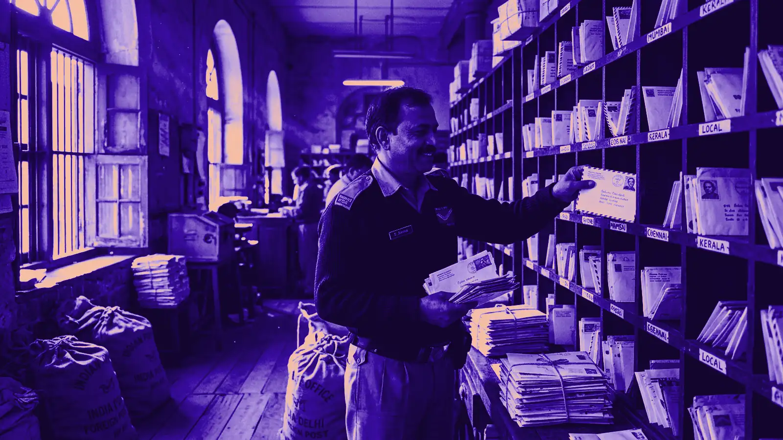A postal worker sorting letters on wooden shelves in a mail room